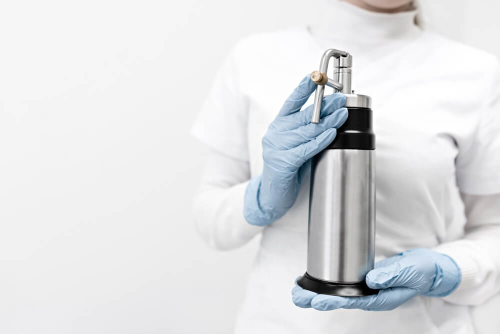 Gloved hands holding stainless steel whipped-cream dispenser